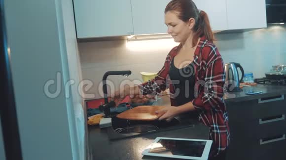 女孩在厨房的砧板上洗碗看着一台数字平板电脑女人在厨房做饭女孩洗了一个视频的预览图