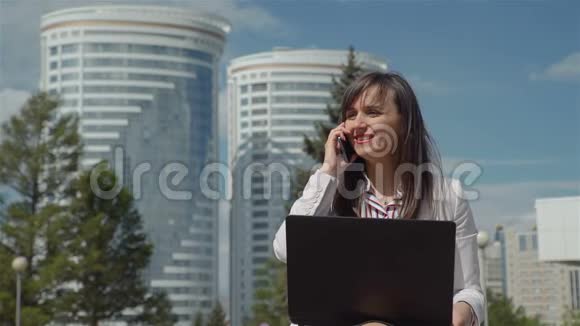 带手提电脑的年轻女子在户外打电话视频的预览图