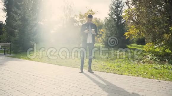 一个年轻人在阳光明媚的秋天公园里用智能手机小巷4K视频的预览图
