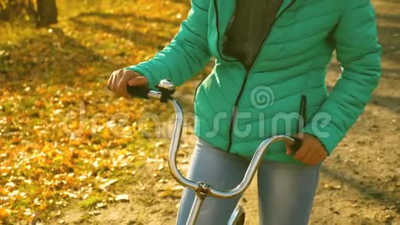女孩的手握着自行车的弯轮小女孩正在秋天的公园里骑自行车上路视频的预览图