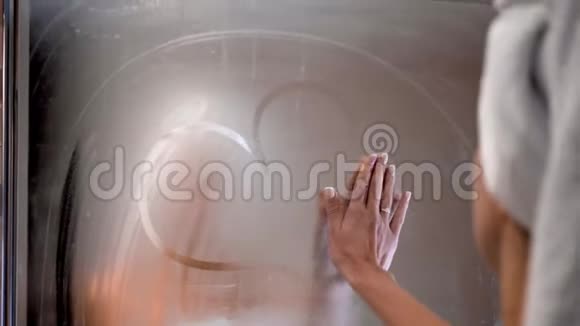 年轻的成年女人在雾蒙蒙的浴室里擦镜子玻璃洗澡后看着朦胧的倒影空气中弥漫着浓浓的水汽视频的预览图