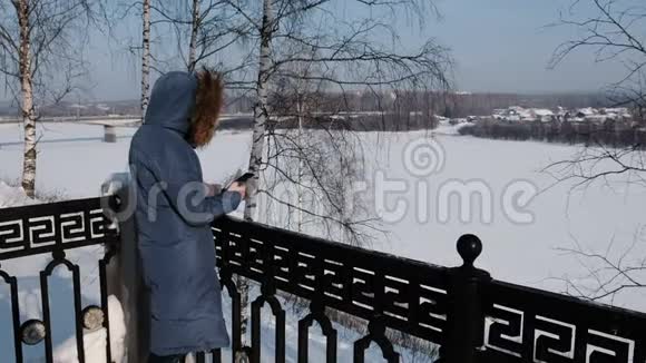 穿着蓝羽绒服的女人在冬天公园的手机里写短信视频的预览图