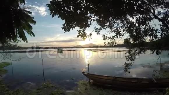漂浮的渔夫停泊在湖湾的木船上日落视频的预览图