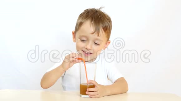快乐的孩子通过吸管喝果汁喝鸡尾酒坐在桌子旁在白色背景上微笑视频的预览图