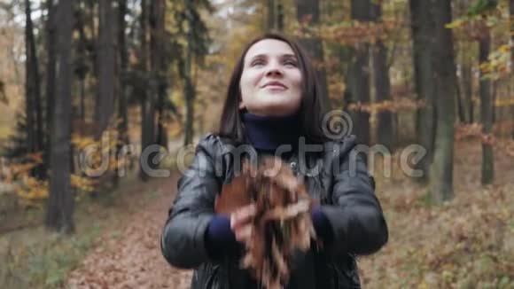 一位快乐的年轻女子在森林里玩秋叶的肖像视频的预览图