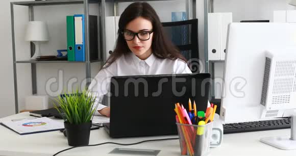 戴着黑色眼镜的女商人在现代办公室用笔记本电脑工作视频的预览图