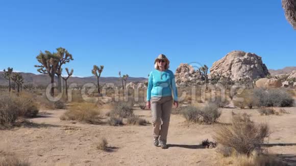 在仙人掌乔舒亚树和巨石阵的沙漠中女游客漫步视频的预览图