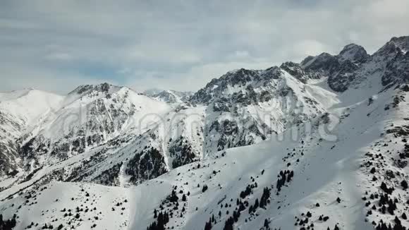 一次平稳的飞行飞越雪山与森林冬景观石山中的雪和天空中的阴沟视频的预览图