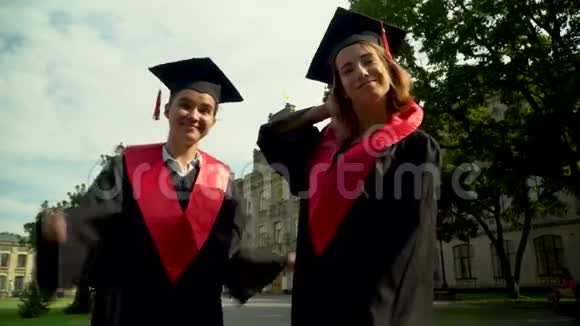 两个快乐的学生穿着黑色和红色的壁炉庆祝他们在大学大楼前毕业二视频的预览图
