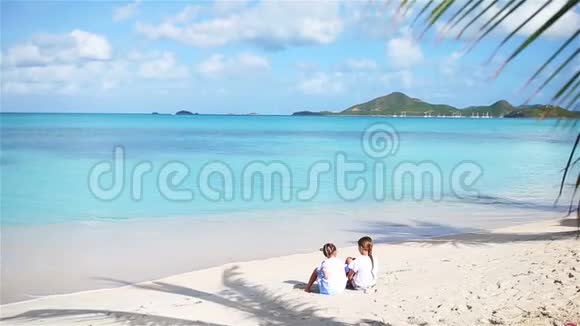沙滩上的两个小女孩快乐的孩子坐在热带海滩棕榈树下视频的预览图