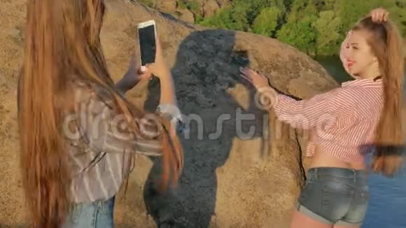 两个年轻的女朋友带着智能手机在岩石上视频的预览图