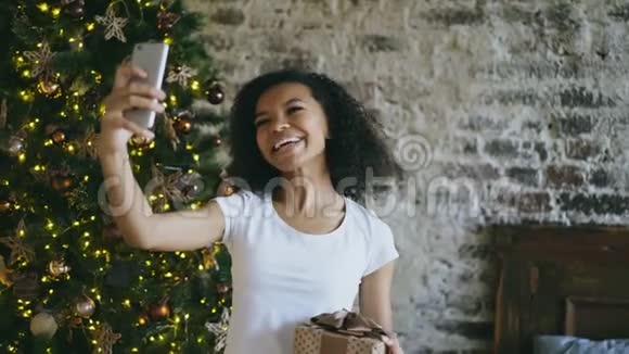 在圣诞树附近的家中使用智能手机摄像头在线聊天的柯里蒂少女视频的预览图