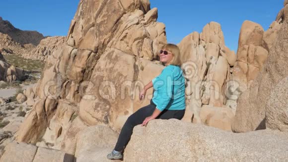 活跃的女人在岩石的边缘高坐欣赏风景和微笑视频的预览图