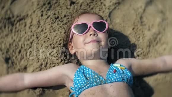 小女孩戴着太阳镜在海滩上日光浴特写脸部视频的预览图