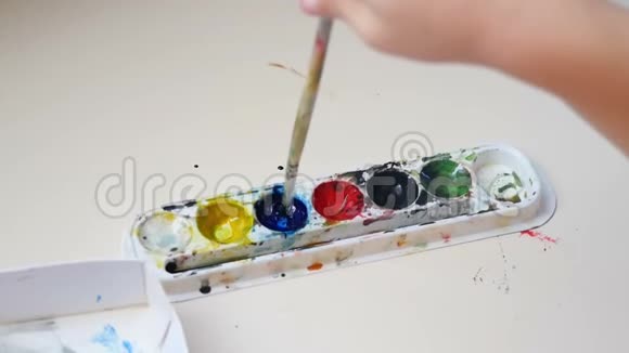 把孩子用水彩画在纸上孩子正在用水彩颜料润湿画笔视频的预览图