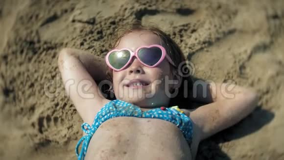 小女孩戴着太阳镜在海滩上日光浴特写脸部视频的预览图
