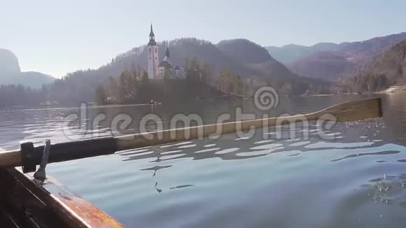 在阳光明媚的一天一只桨在水中划桨在背景中划桨的岛屿湖斯洛文尼亚的布莱德湖视频的预览图