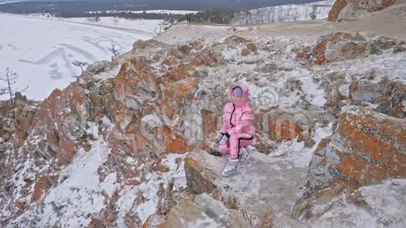 女人坐在山上旅行者正在山顶上散步漂亮的女孩穿着时尚的粉红色羽绒服视频的预览图