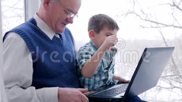 网上购物爷爷带着孩子通过室内笔记本电脑用电子货币计算视频的预览图