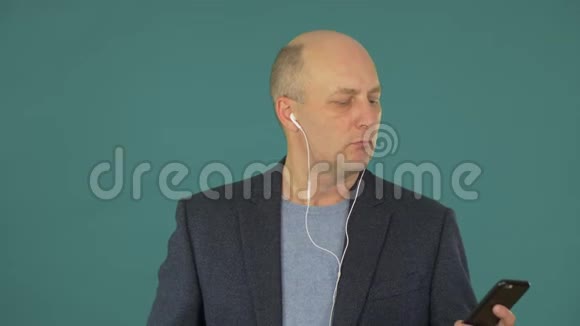 秃顶的中年商人用耳机和智能手机听音乐视频的预览图