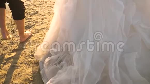 新郎赤脚新娘穿着白色连衣裙沿着河沿海滩散步情侣在沙滩上散步视频的预览图