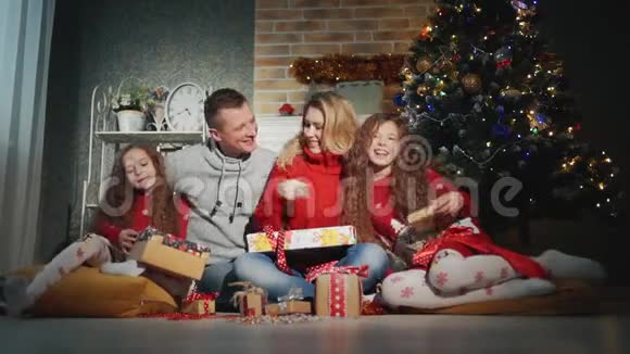 幸福的四口之家正微笑着望着圣诞树脚下的摄像机视频的预览图