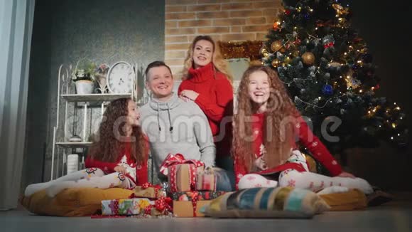 幸福的四口之家正微笑着望着圣诞树脚下的摄像机视频的预览图