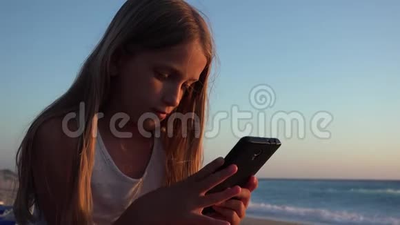 孩子在玩智能手机日落时在海滩上玩女孩在玩平板电脑视频的预览图