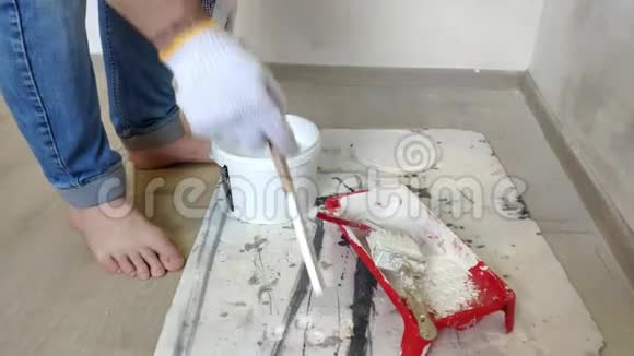 一个头发花白的留着胡须的人用棍子把白色的油漆混合在桶里然后倒进容器里视频的预览图