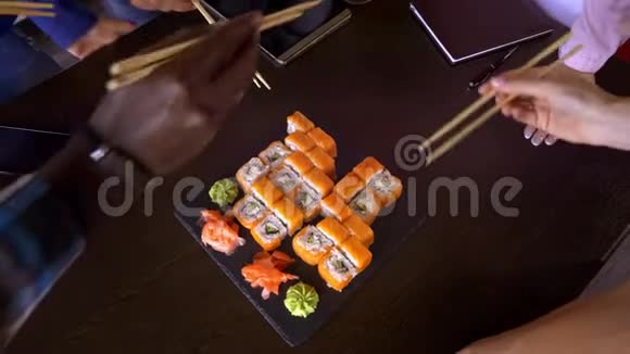 在餐馆的桌子上放一套寿司卷一群朋友用竹棒吃寿司卷视频的预览图