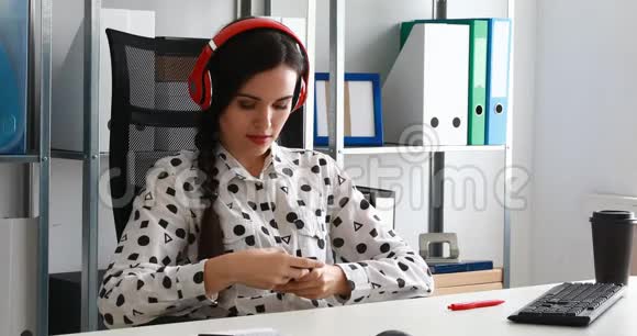 女商人戴着红色耳机在现代办公室的智能手机上拍摄视频视频的预览图