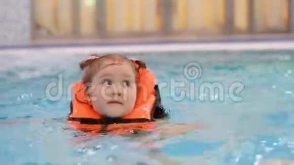 穿着救生衣在游泳池里的小女孩学会游泳在水里游泳的婴儿视频的预览图
