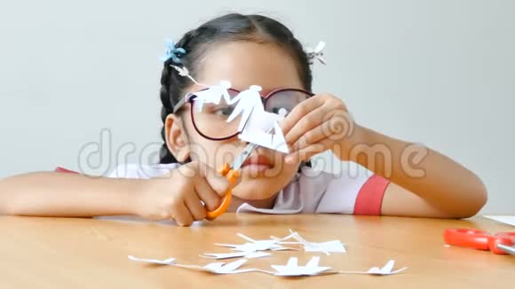 亚洲小女孩在泰国幼儿园穿学生制服用剪刀剪白纸使家庭形状父亲儿子视频的预览图