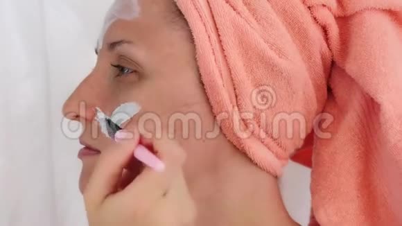 年轻女人用刷子在脸上涂化妆品面膜女孩在她的脸颊上涂了一个面罩女孩做她的脸视频的预览图