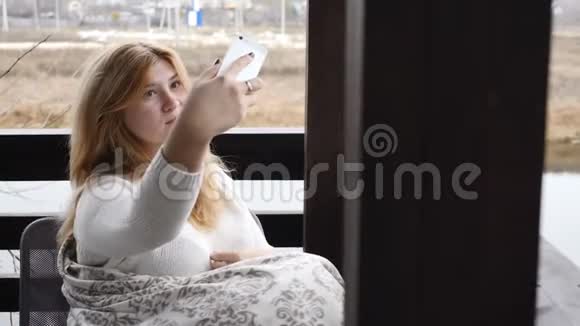 舒适的家居概念年轻女子坐在格子呢的开放式露台上自拍她手里拿着一杯咖啡微笑视频的预览图