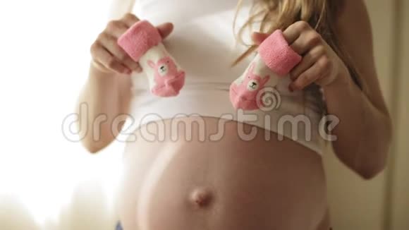 怀孕的金发女人在肚子上玩粉色婴儿靴快关门视频的预览图