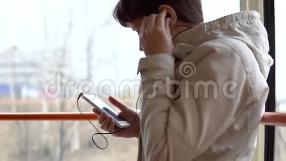 一个女人坐电车在智能手机上听耳机里的音乐视频的预览图