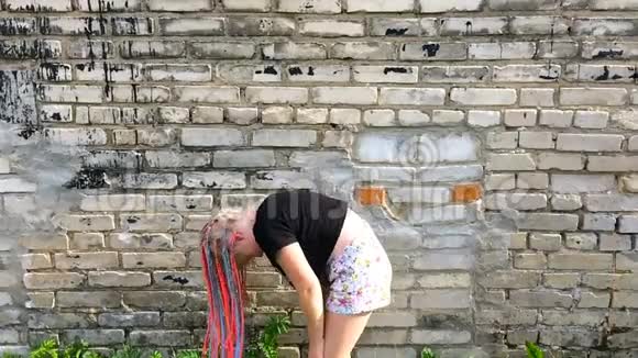 时髦女孩在砖墙附近挥舞非洲辫子慢动作视频的预览图