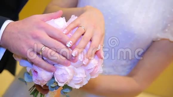 新婚夫妇手里拿着结婚戒指新娘和新郎在鲜花或婚礼花束上戴着结婚戒指新婚夫妇视频的预览图