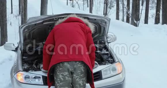 看着汽车发动机的人修理破车的人冬天开车麻烦在一条下雪的乡村道路上视频的预览图