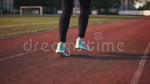女人脚穿运动鞋特写那个女孩在体育场沿着跑道跑后面的景色慢动作视频的预览图