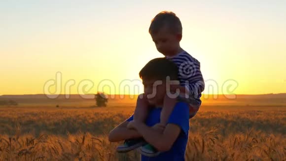 两个男孩在日落时在一片麦田里玩着金色的小穗一个男孩坐在另一个男孩的肩膀上视频的预览图