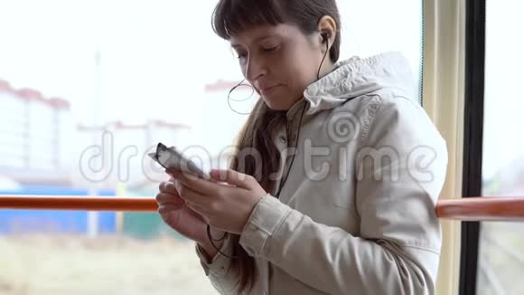 一个女人坐电车在智能手机上听耳机里的音乐视频的预览图