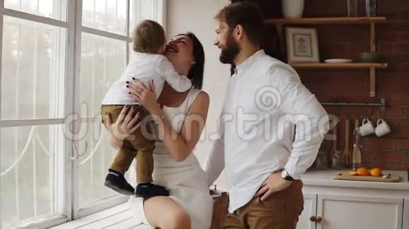 年轻的母亲抱着她可爱的儿子和年轻的父亲一起坐在窗台上窗户上装饰着视频的预览图
