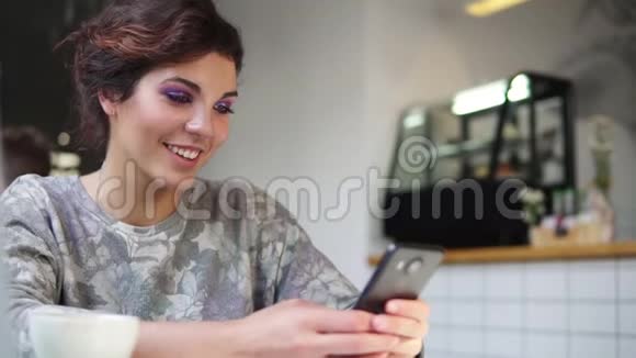 在咖啡馆里用她的手机观看美丽的年轻女性微笑着在咖啡馆里使用智能手机的女人视频的预览图