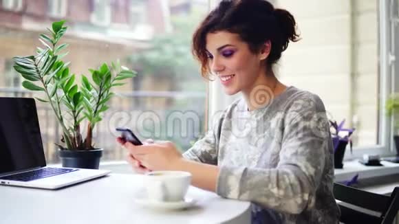 美丽的年轻女子在咖啡馆里用她的手机和微笑的特写镜头在咖啡馆里使用智能手机的女人视频的预览图