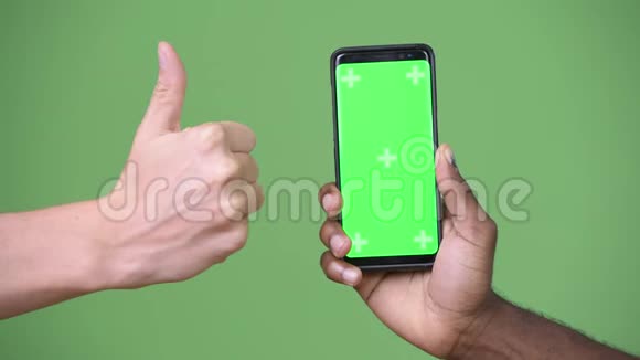 两只多民族的手在竖起大拇指的同时显示手机视频的预览图