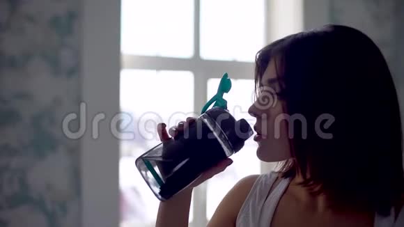 健身妇女从瓶子里喝水肌肉发达的年轻女性在健身房休息锻炼视频的预览图