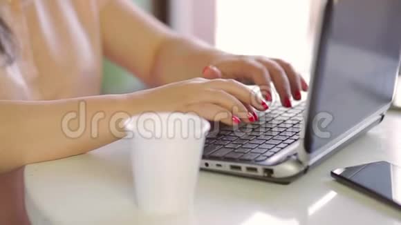 女性手在笔记本电脑上特写打印文本用一次性杯子喝饮料视频的预览图