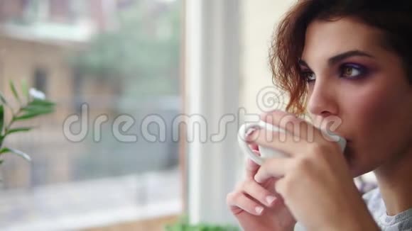 美丽的年轻女子在窗外喝着热咖啡做梦特写镜头慢镜头视频的预览图